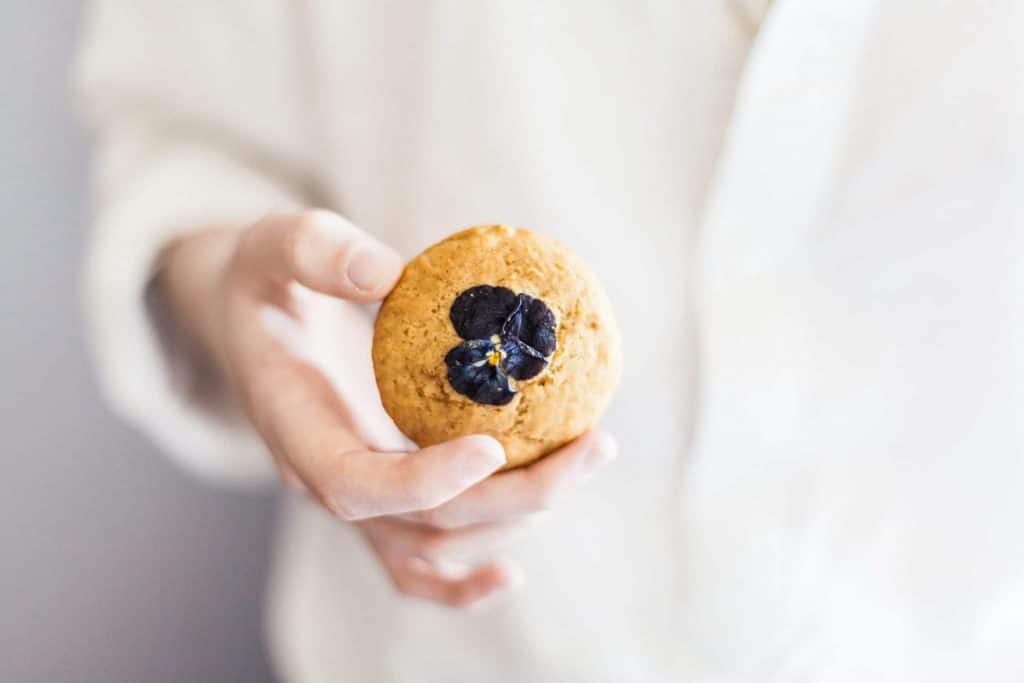 Chef with white coat holding a tan colored muffin with flower on top