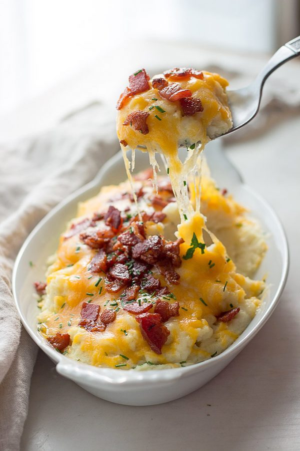 mashed cauliflower topped with bacon, cheese, and parsley with one bite on a spoon