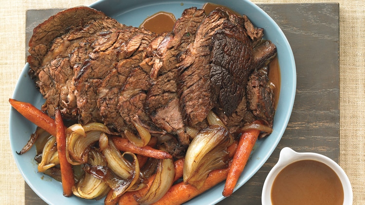 pot roast, onions, carrots on a blue serving plate with gravy on the side