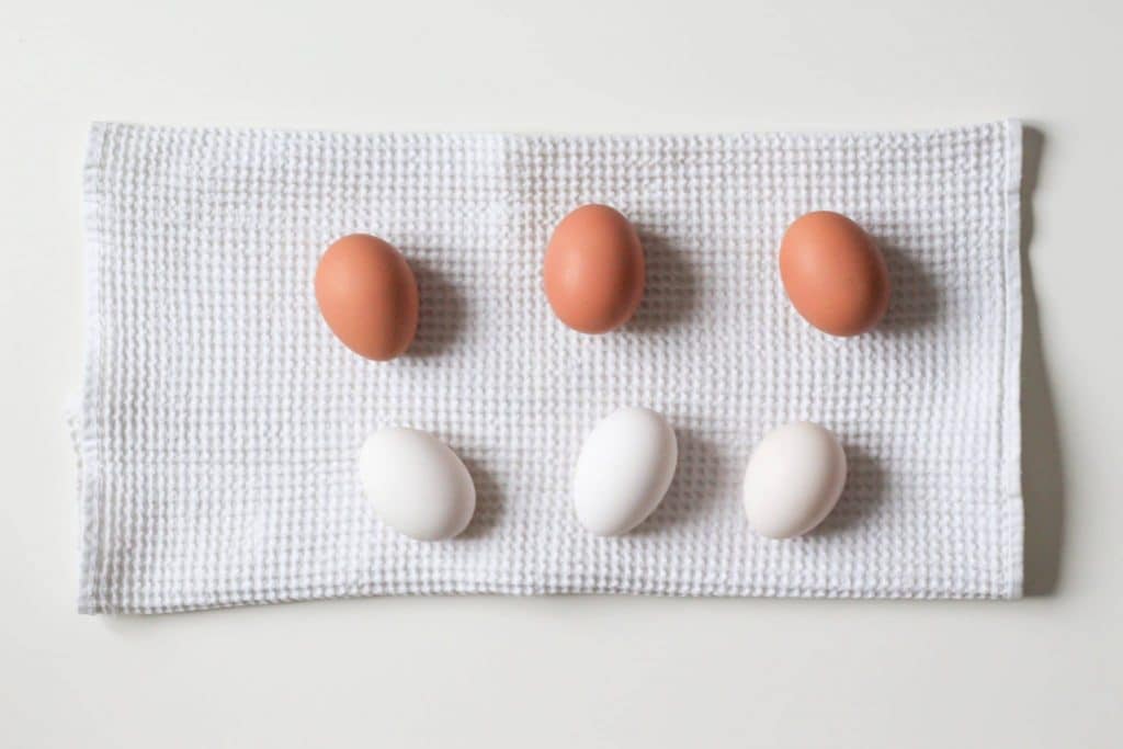 Three brown eggs and three white eggs on a white kitchen waffle towel on white background