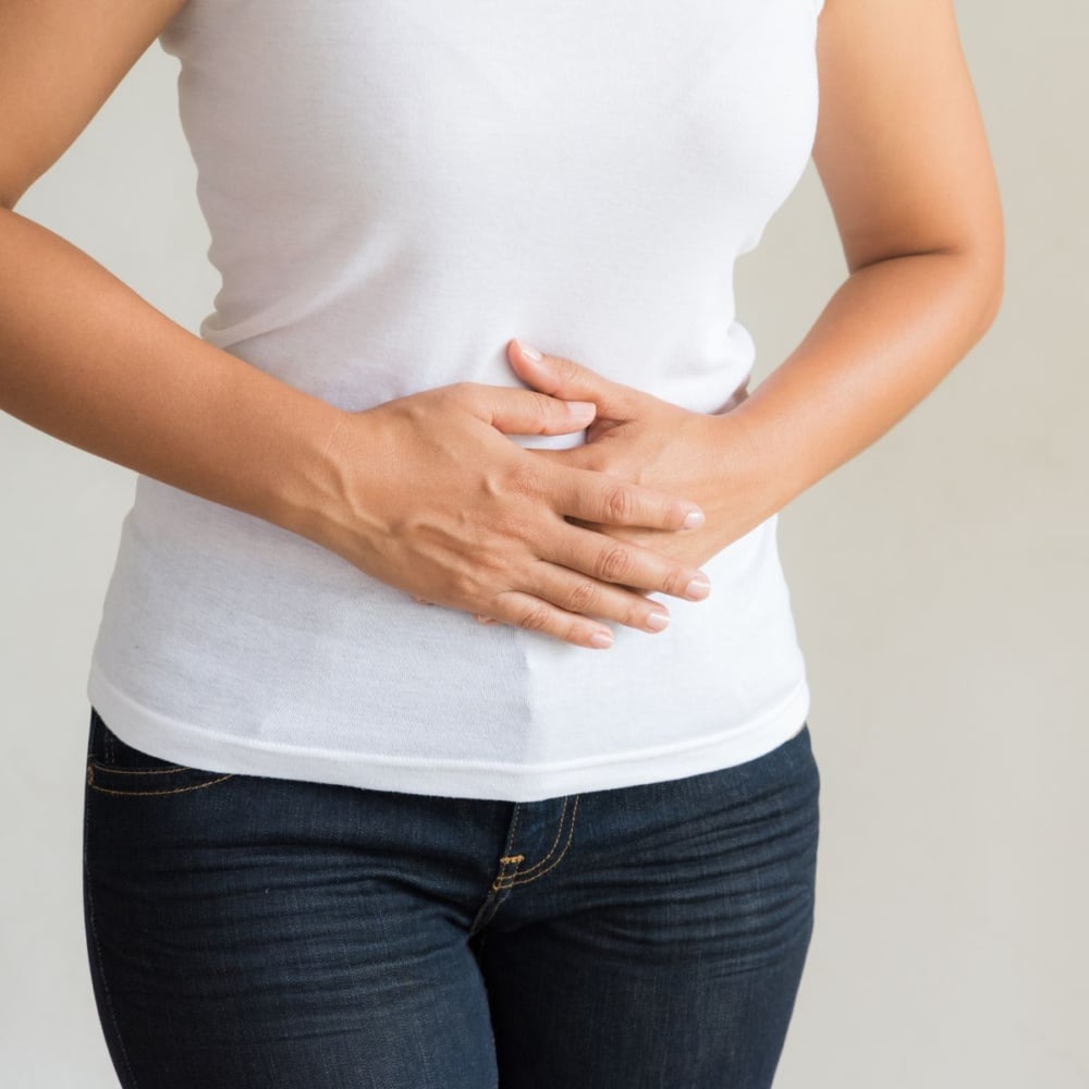 woman holding stomach in a white shirt and jeans