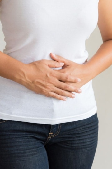 woman holding stomach in a white shirt and jeans