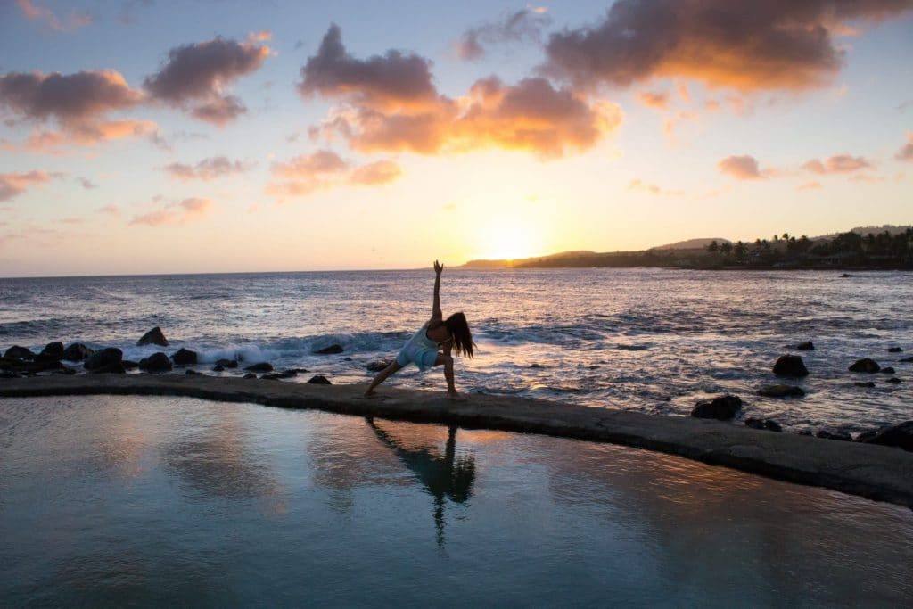 A woman doing yoga at sunset in a white dress on the side of a pool out of a funk