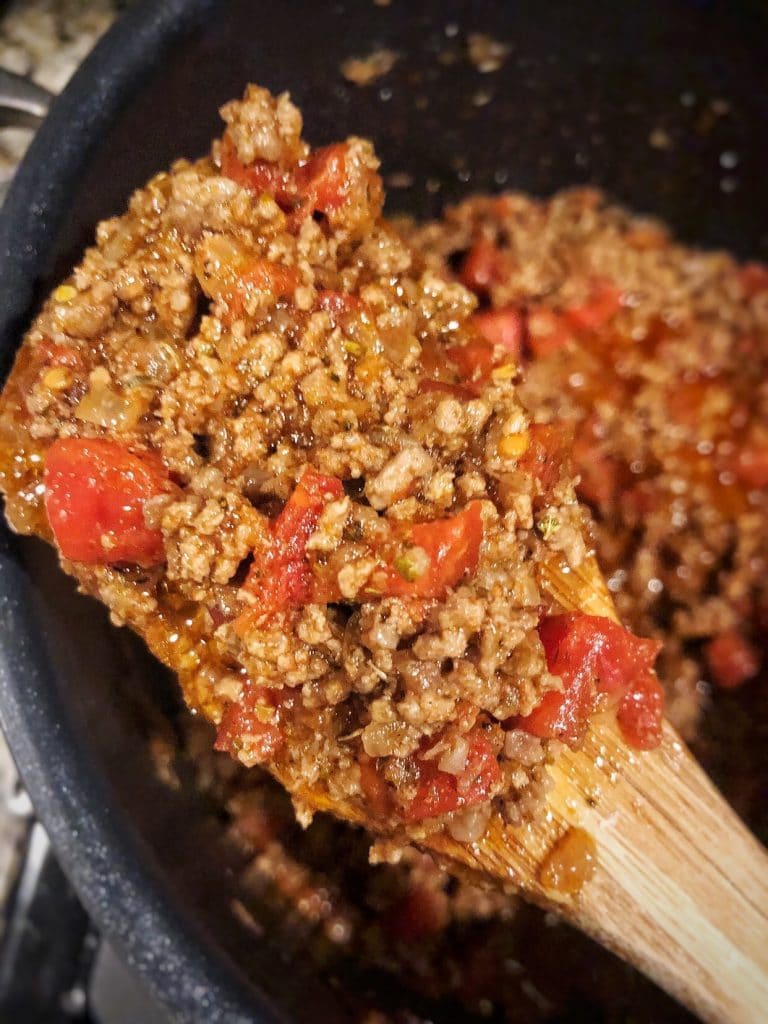 close-up of chili with tomatoes in large pot on wooden spoon