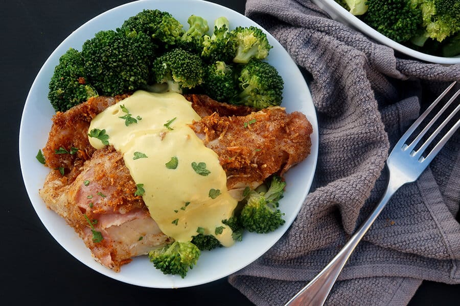 chicken cordon bleu with yellow sauce, parsley and broccoli with kitchen towel and fork nearby