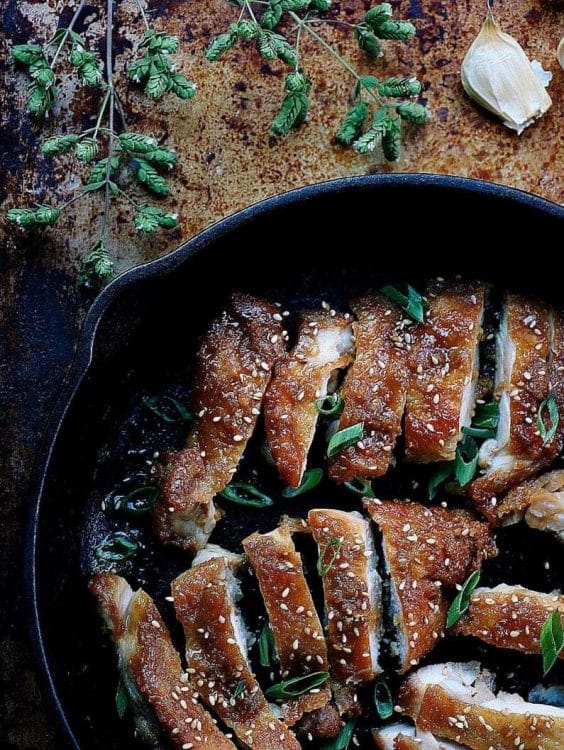 chicken teriaki in an iron skillet topped with sesame seeds and chopped green onions