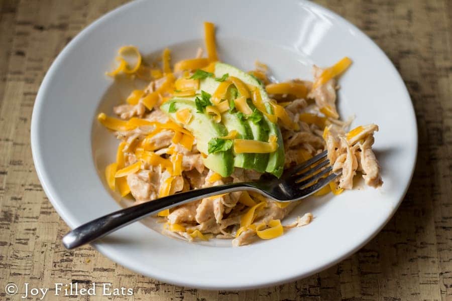 salsa chicken in a white bowl topped with avocado slices and shredded cheddar cheese