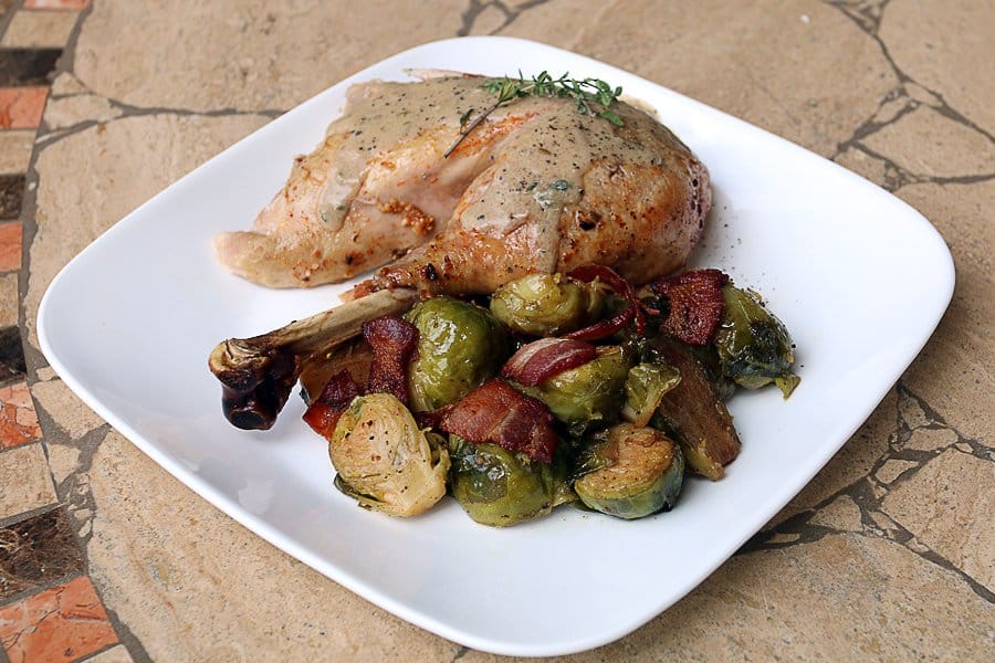 turkey leg topped with rosemary with brussels sprouts and bacon on white plate