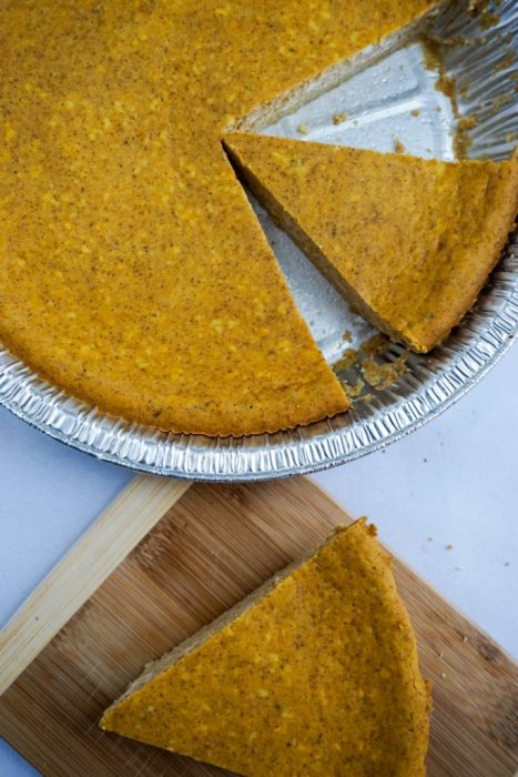 pumpkin pie sliced in aluminum pie tin with another slice nearby on a cutting board