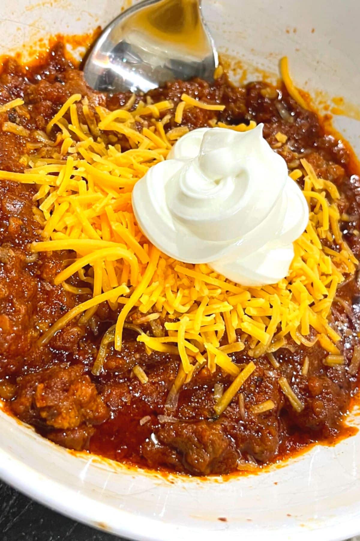 keto chili with cheddar cheese and sour cream in white bowl with a spoon