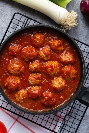 meatballs in a skillet on a cooling rack with ingredients like onions and tomatoes around it for keto meal prep idea
