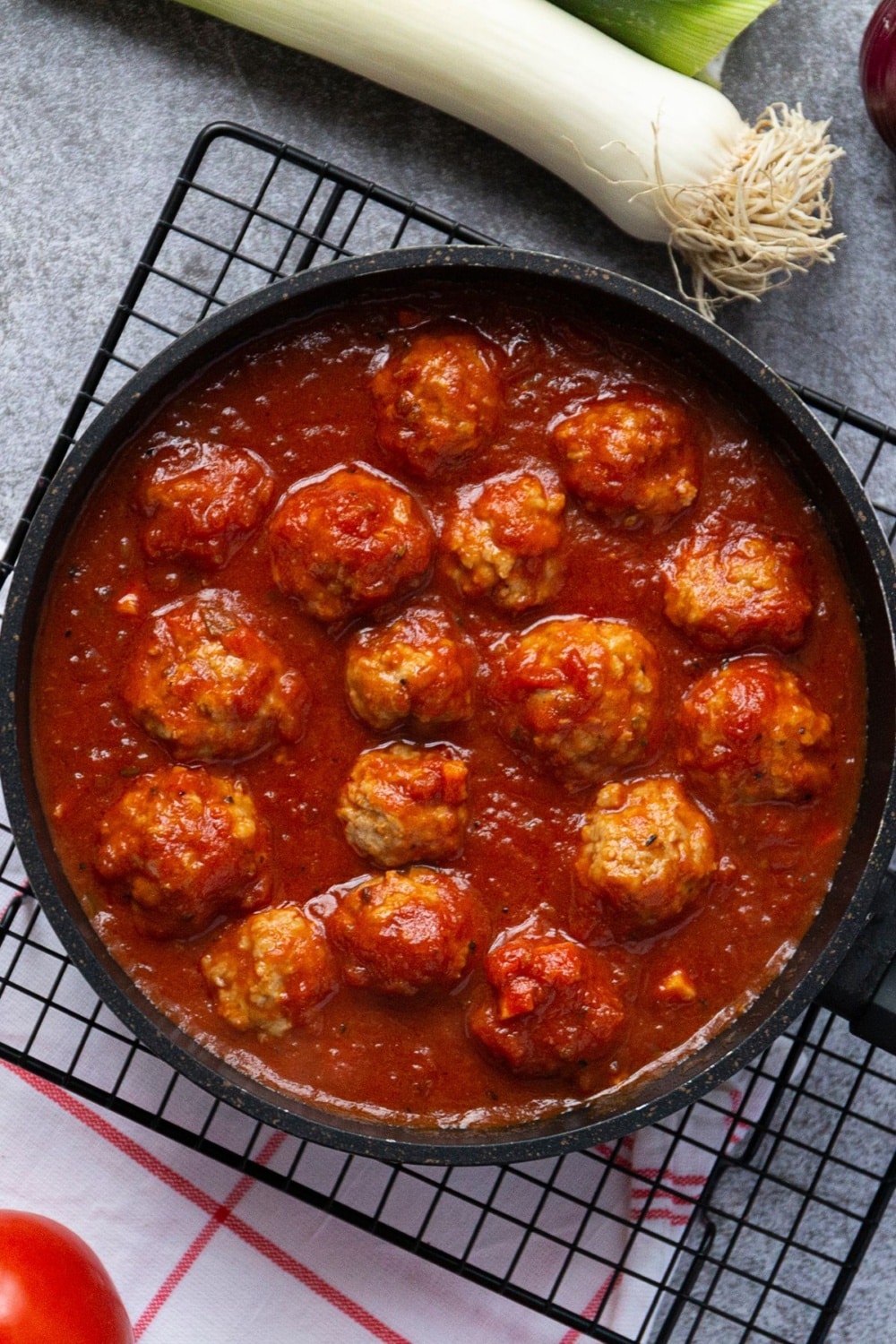 meatballs in a skillet on a cooling rack with ingredients like onions and tomatoes around it for keto meal prep idea