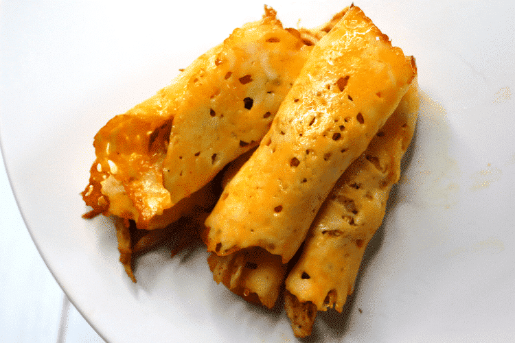 four taquitos on a white plate overhead view