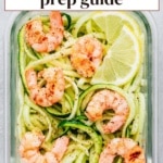 Overhead view of shrimp zoodles meal prep with lemon and lime wedges in a glass container.
