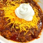 Overhead shot of keto chili topped with shredded cheddar cheese and a dollop of sour cream in a white bowl