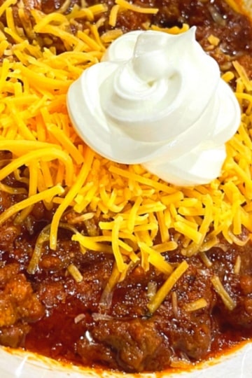 Overhead shot of keto chili topped with shredded cheddar cheese and a dollop of sour cream in a white bowl