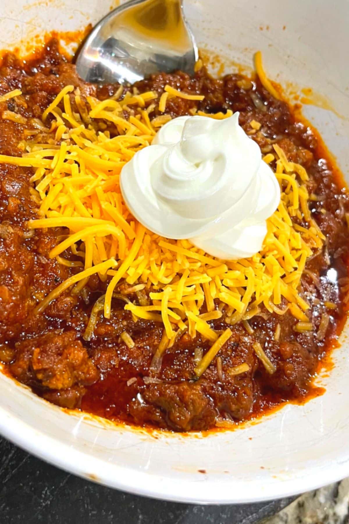 Overhead shot of keto chili topped with shredded cheddar cheese and a dollop of sour cream in a white bowl