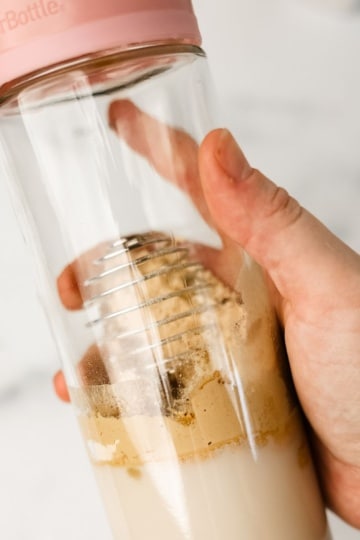 hand holding a blender bottle full of keto meal replacement shake ingredients getting ready to shake it up