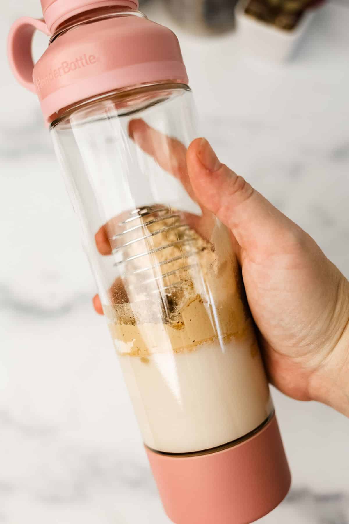 hand holding a blender bottle full of keto meal replacement shake ingredients getting ready to shake it up