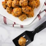 Single sausage ball on a spatula with mound of sausage balls in the background