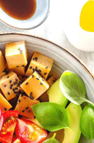 A colorful, appetizing bowl of assorted vegan keto foods, including leafy greens, avocado slices, cherry tomatoes, crunchy nuts and seeds, and a hearty scoop of tofu or tempeh, drizzled with a rich, creamy dressing, showcasing the diversity and deliciousness of a plant-based ketogenic meal.