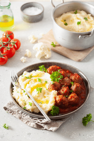 Deliciously cooked meatballs garnished with fresh herbs, served alongside creamy mashed cauliflower on a white plate