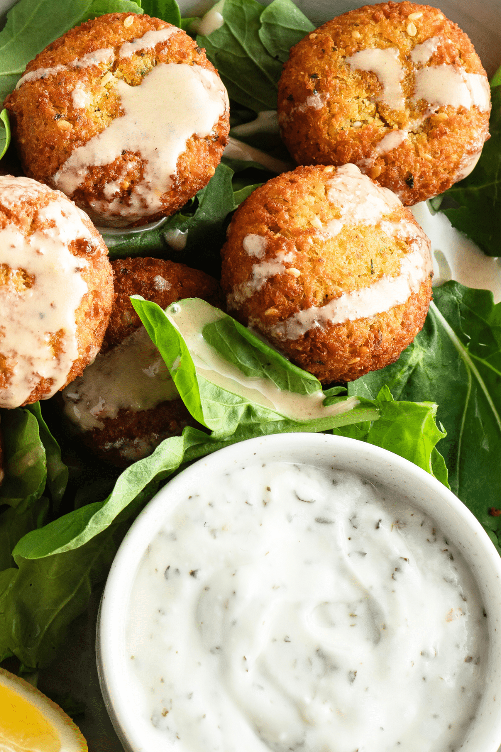 A delicious image of golden-brown baked falafel resting on a bed of fresh greens. These flavorful chickpea-based patties are perfectly crispy on the outside and tender on the inside. The falafel is accompanied by a colorful assortment of lettuce, tomatoes, cucumbers, and a drizzle of creamy tahini sauce. This appetizing and vegetarian-friendly dish is a feast for the eyes and promises a delightful burst of Mediterranean flavors. 