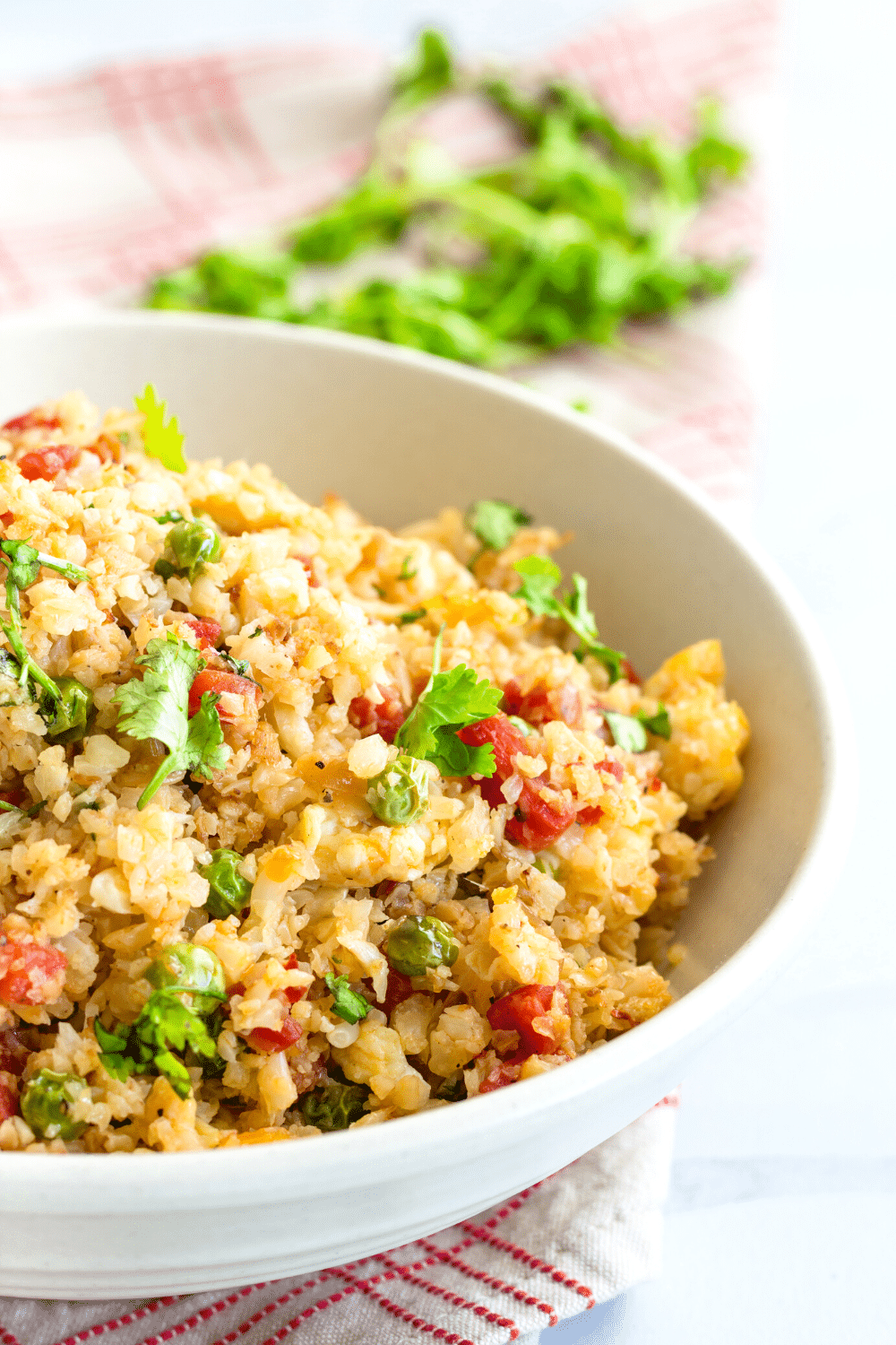 A colorful bowl of cauliflower fried rice bursting with vibrant vegetables, herbs, and spices. The cauliflower rice, made from finely chopped cauliflower florets, is stir-fried to perfection and mixed with an assortment of diced carrots, bell peppers, peas, and scallions. The dish is seasoned with a medley of aromatic spices and sauces, creating a flavorful and nutritious alternative to traditional fried rice. The colorful vegetables add visual appeal to this low-carb, gluten-free, and healthy dish