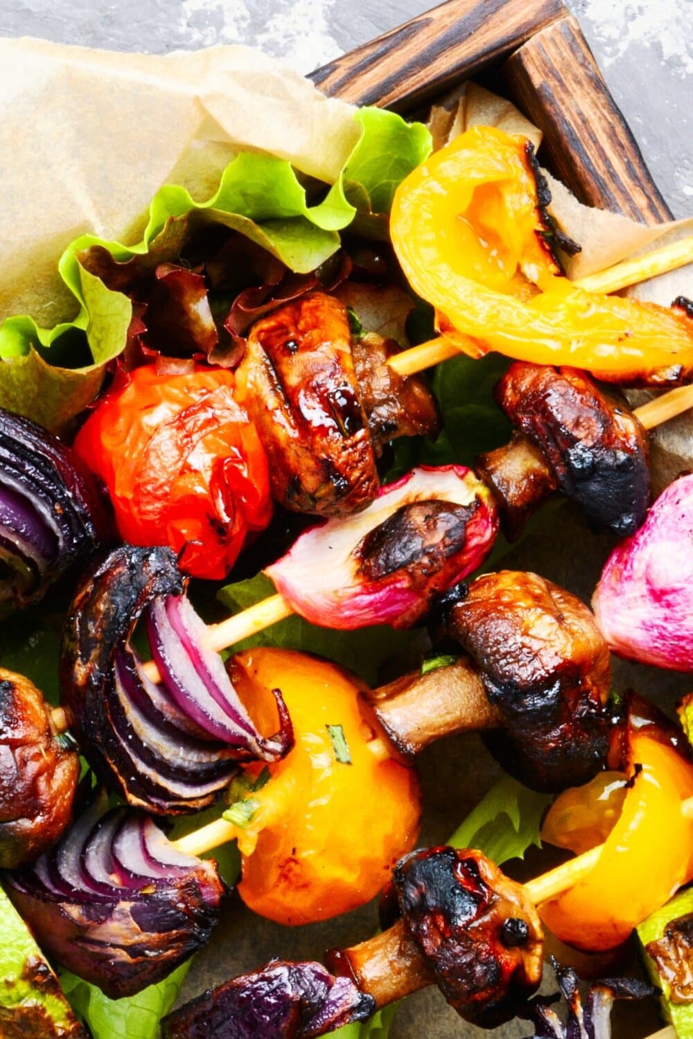 Colorful vegetable skewers with chunks of red bell pepper, white onion, juicy tomato, and earthy mushroom, arranged neatly on a rustic wooden tray lined with brown parchment paper, emphasizing a vibrant, healthy, and keto-friendly grilling option.