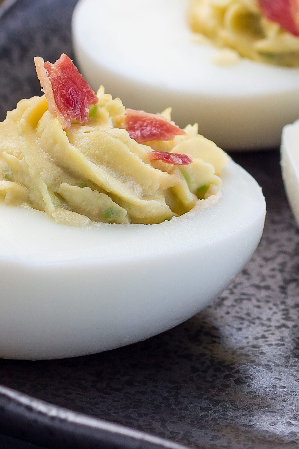 Closeup shot of avocado bacon deviled eggs, highlighting the creamy avocado filling, topped with crispy bacon bits, inside halved egg whites, showcasing a delicious, keto-friendly twist on a classic appetizer