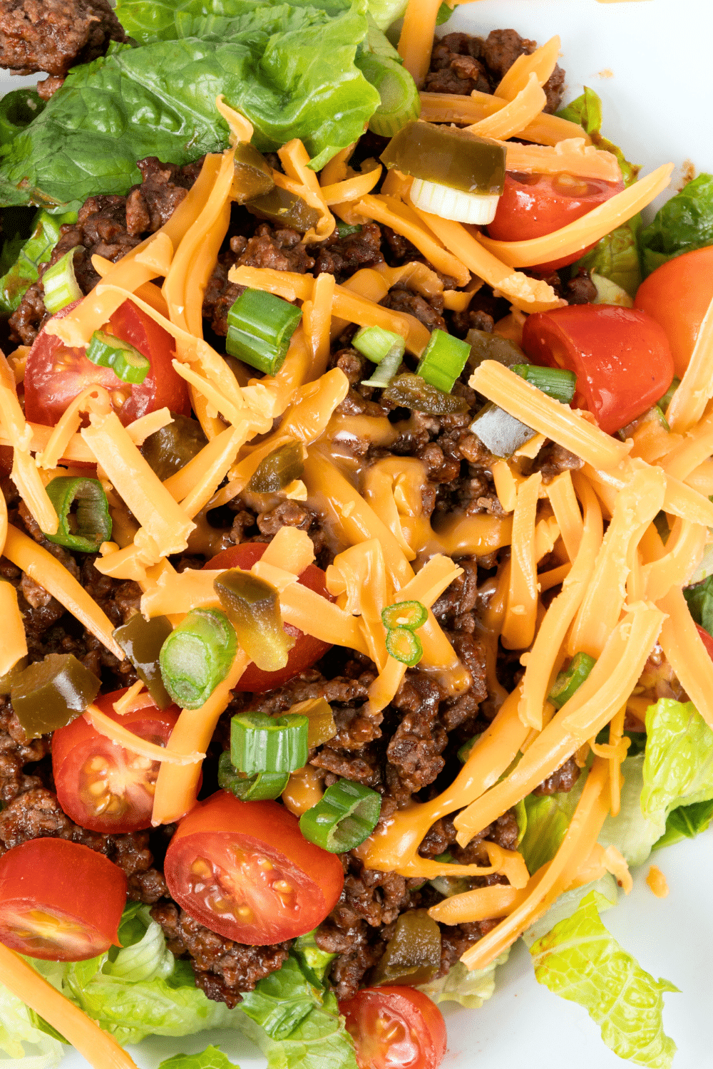 A flavorful salad made with ground beef, shredded cheddar cheese, hot sauce, sour cream, and chopped Romaine lettuce.