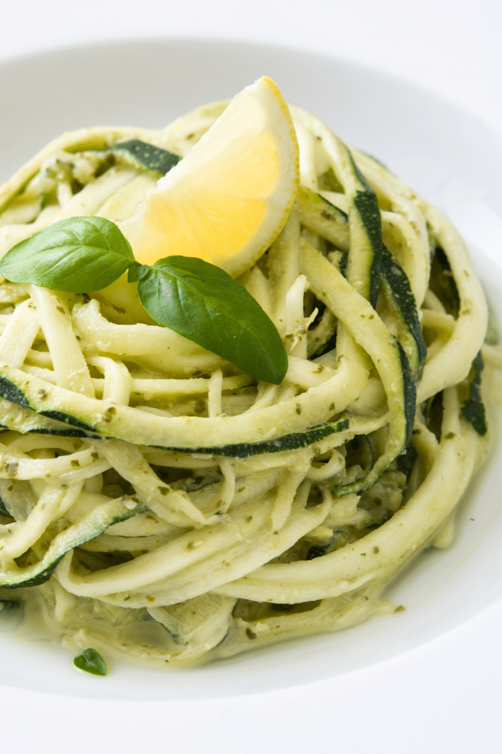 Close-up of a colorful plate of zoodles (zucchini noodles) cooked to perfection and delicately coated with a rich and velvety creamy garlic Parmesan sauce. The vibrant green zoodles intertwine gracefully, creating a visually appealing presentation that is both appetizing and satisfying