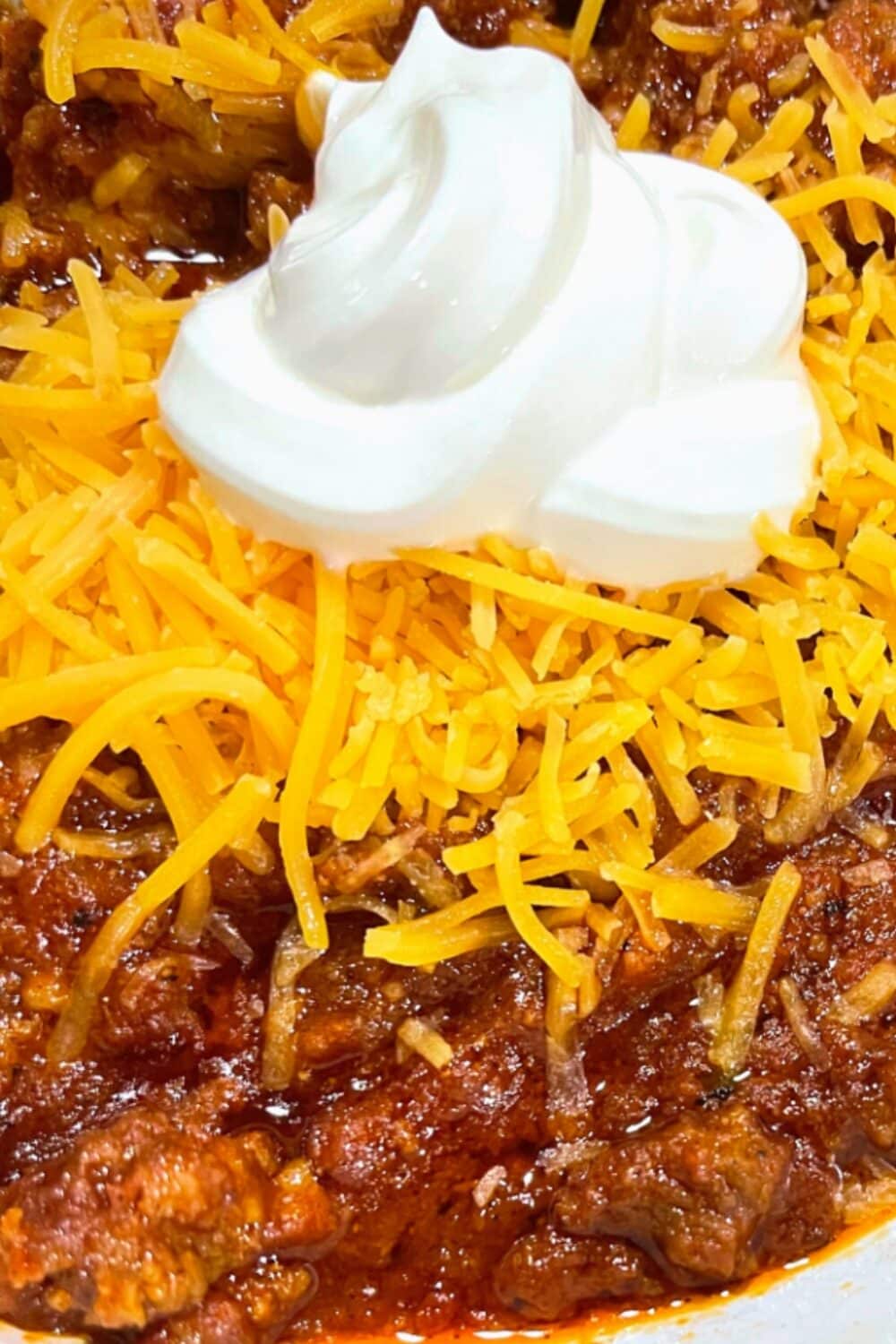 "Steaming bowl of hearty keto chili, generously topped with a golden layer of melted cheese and a dollop of creamy sour cream. The chili features tender chunks of meat, vibrant bell peppers, and rich spices, creating a warm and comforting dish perfect for a satisfying low-carb meal.