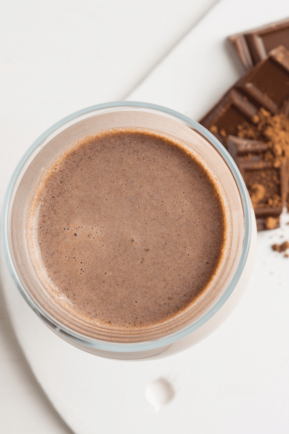 A deep chocolate-colored smoothie in a glass, topped with shaved chocolate and a slice of avocado.