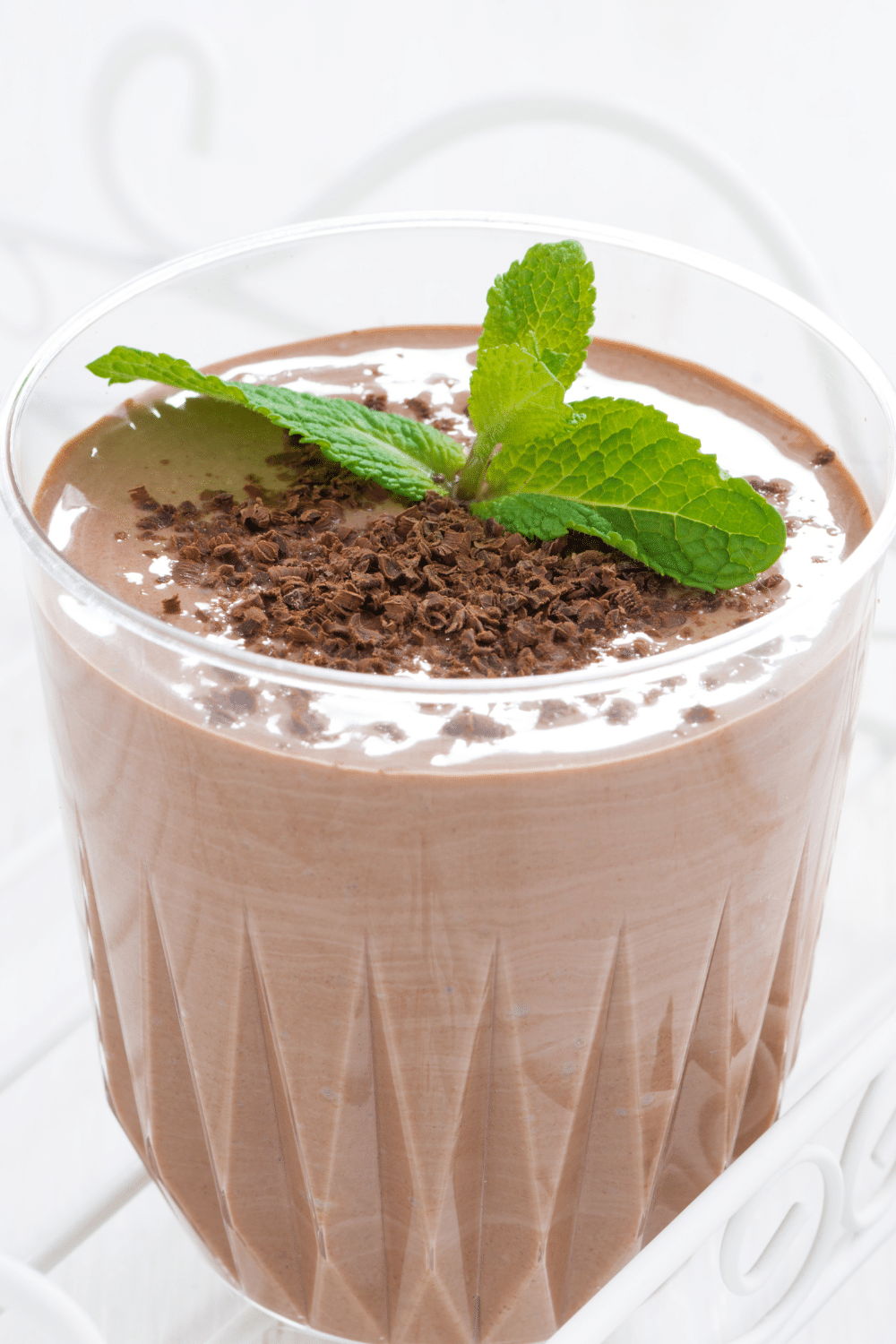 A green-tinted chocolate smoothie in a glass, garnished with fresh mint leaves and cacao nibs.
