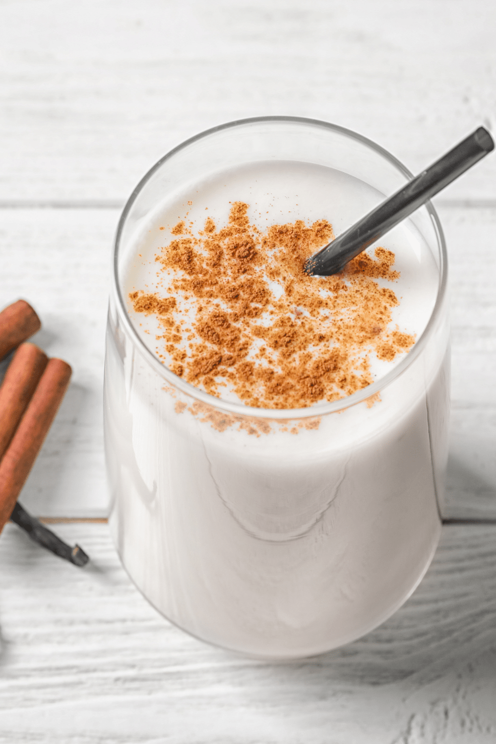 A beige-colored smoothie in a glass, sprinkled with ground cinnamon and flax seeds.