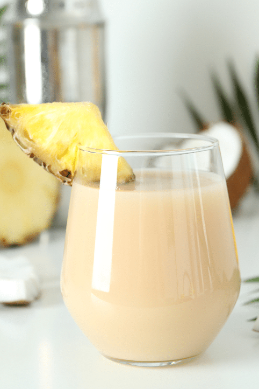 A creamy white smoothie in a glass, garnished with a slice of pineapple and a sprinkle of shredded coconut.