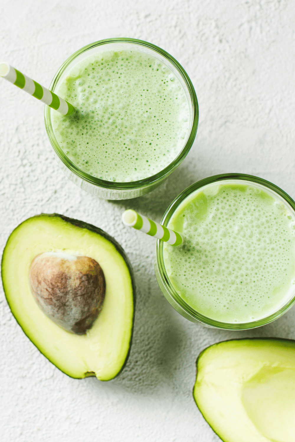 A creamy pale green avocado smoothie in a glass, adorned with a slice of ripe avocado.