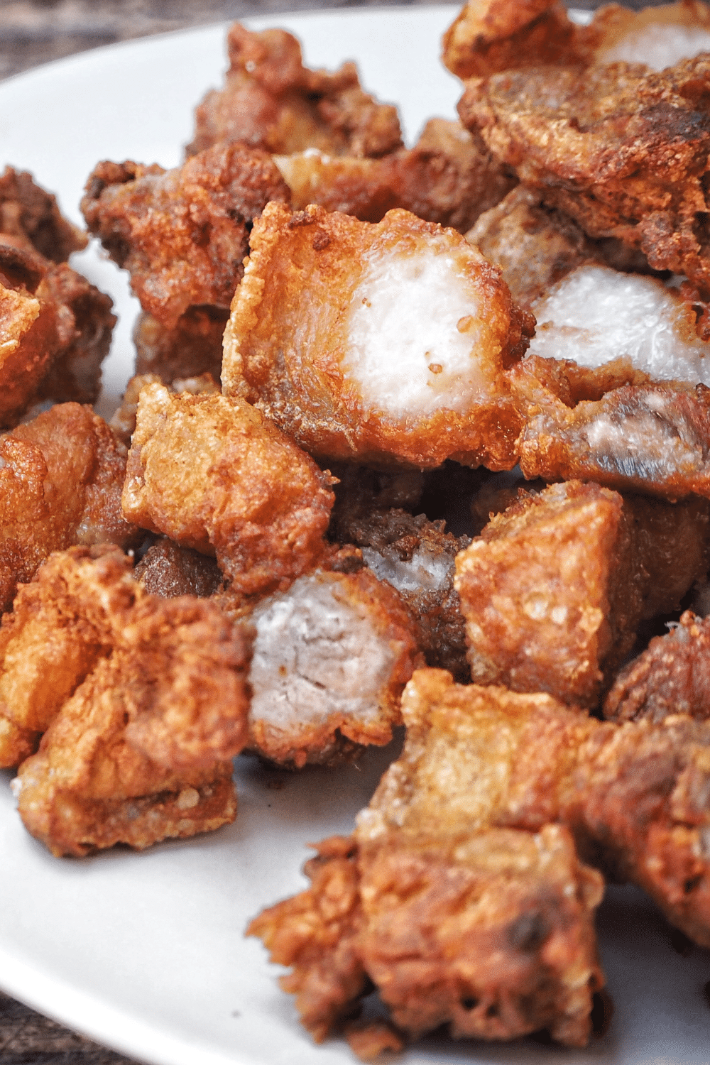 An exquisite dish of perfectly cooked crispy pork belly takes center stage on a pristine white ceramic plate. The pork belly, boasting a glorious golden-brown hue, is expertly scored to create a beautiful crosshatch pattern, allowing the glistening fat to render and the skin to achieve a satisfying crunch. The edges are slightly caramelized, hinting at the delightful contrast of textures and flavors to come. The succulent pork belly rests atop a bed of finely julienned fresh greens, adding a pop of vibrant color to the presentation. The dish is garnished with a sprinkle of finely chopped fresh herbs, enhancing the visual appeal and lending a delightful herbal aroma to the air. Wisps of steam gently rise from the mouthwatering masterpiece, enticing the senses with its irresistible aroma. The dish promises an indulgent experience, featuring a harmonious blend of tender, melt-in-your-mouth meat and a tantalizing crispy exterior that is sure to captivate any food lover's heart and palate.