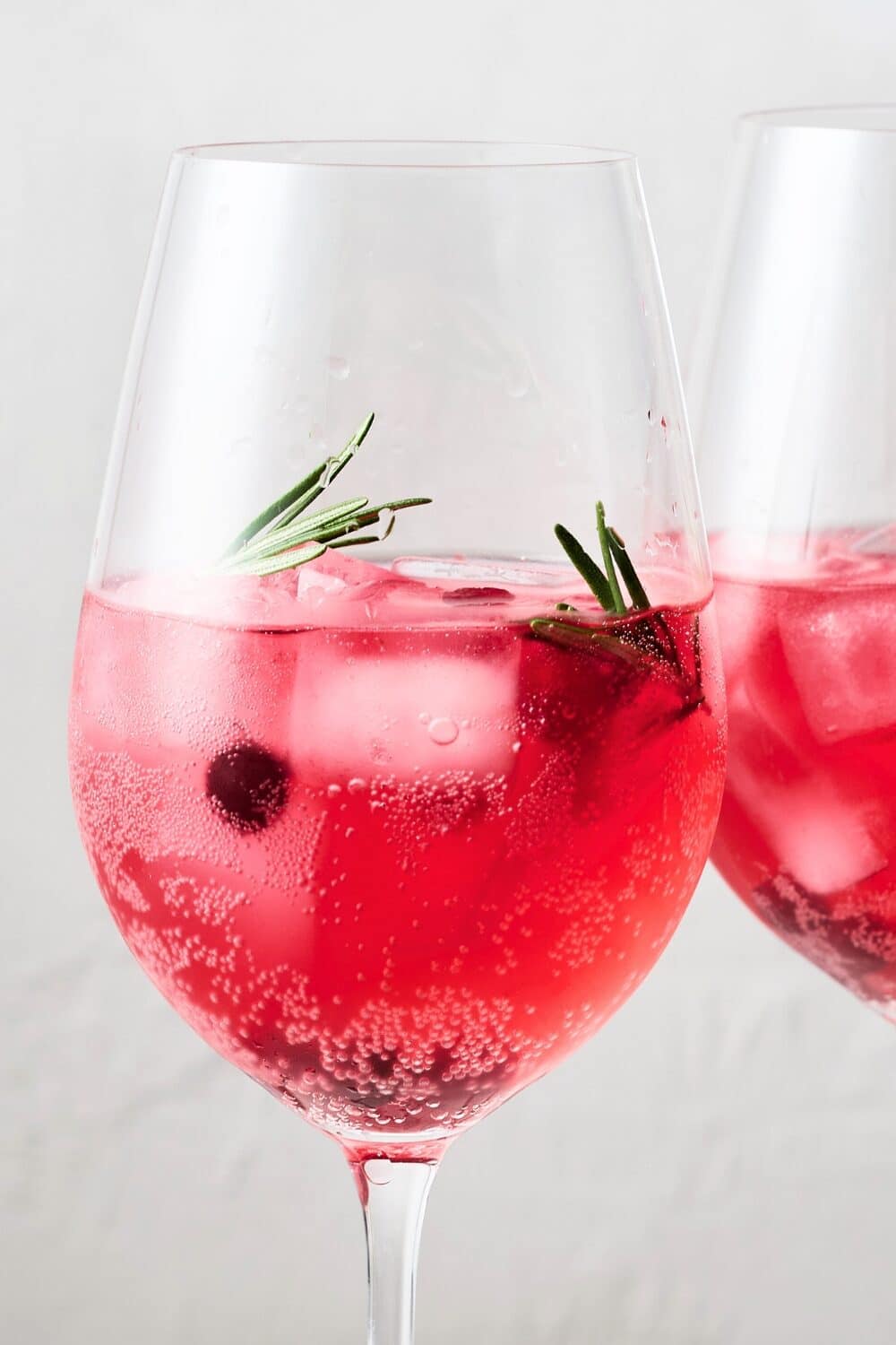 A wine glass showcasing a fizzy cranberry spritzer, adorned with fresh cranberries and a lime wedge and rosemary sprigs.