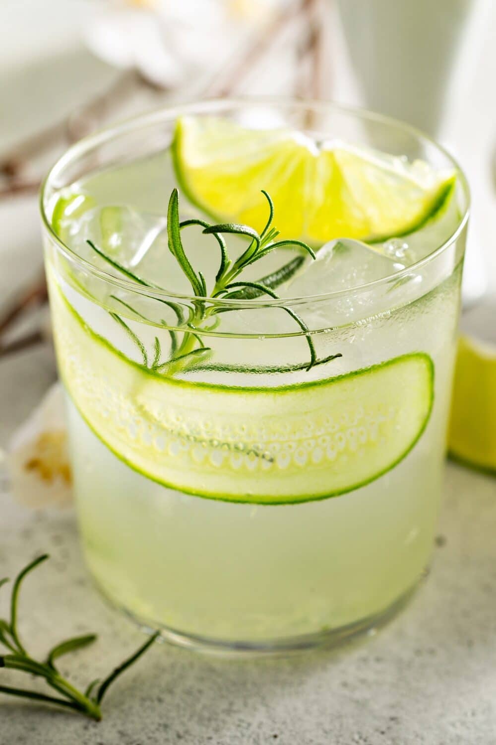 A clear glass filled with a refreshing cucumber gimlet mocktail, garnished with a cucumber slice and lime wedge.
