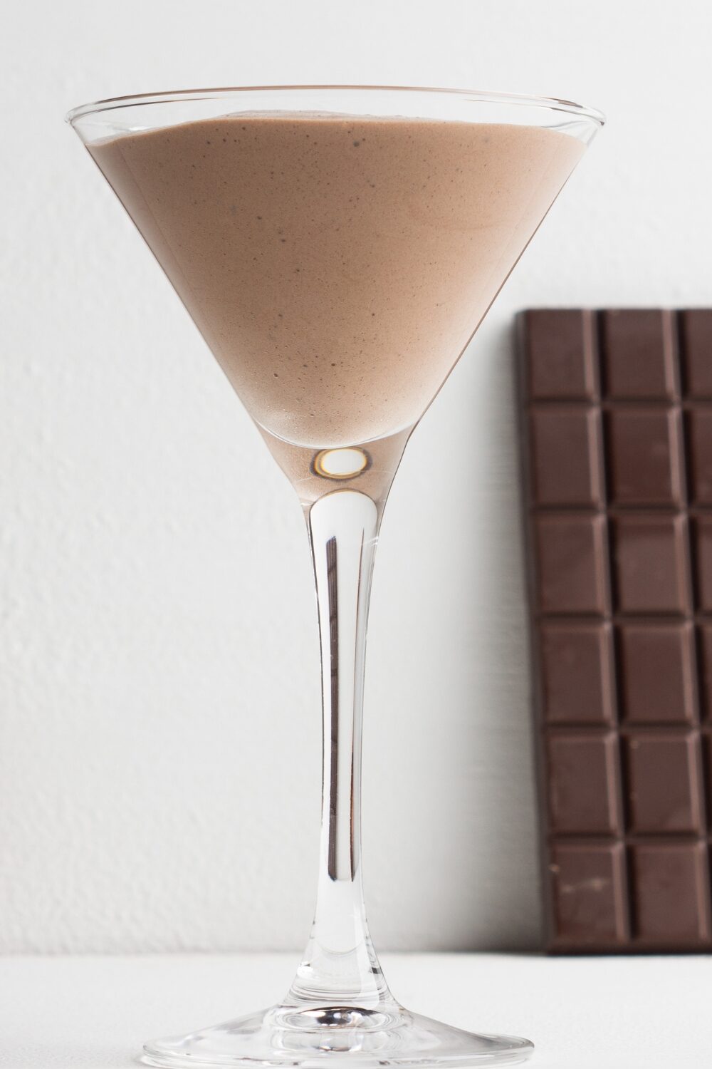 A sleek martini glass holding a velvety chocolate mocktail, sprinkled with dark chocolate shavings on top.