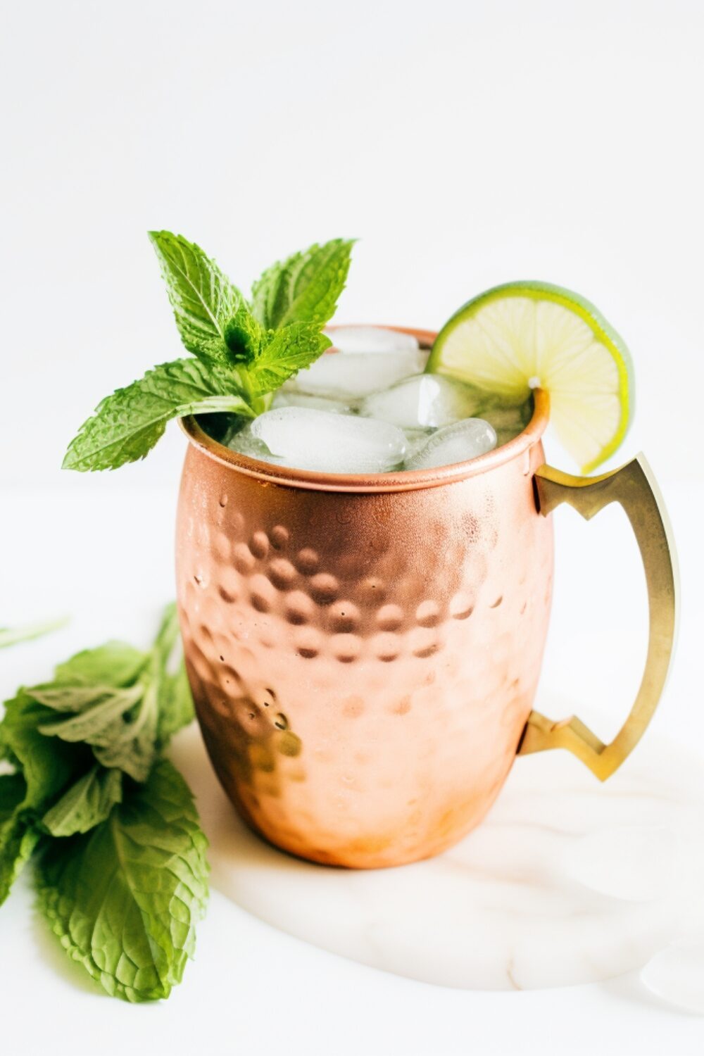 A traditional copper mule mug filled with a fizzy lime mocktail, garnished with a lime wedge and fresh mint sprig.
