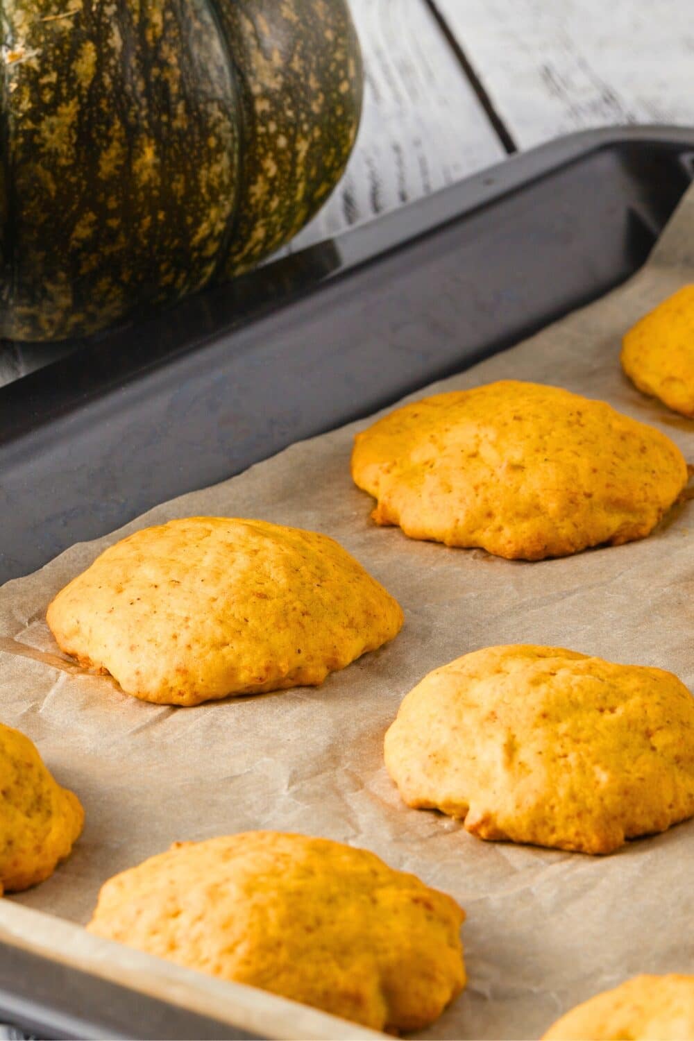 Freshly baked pumpkin cookies on a cooling rack, with a green pumpkin in the background.