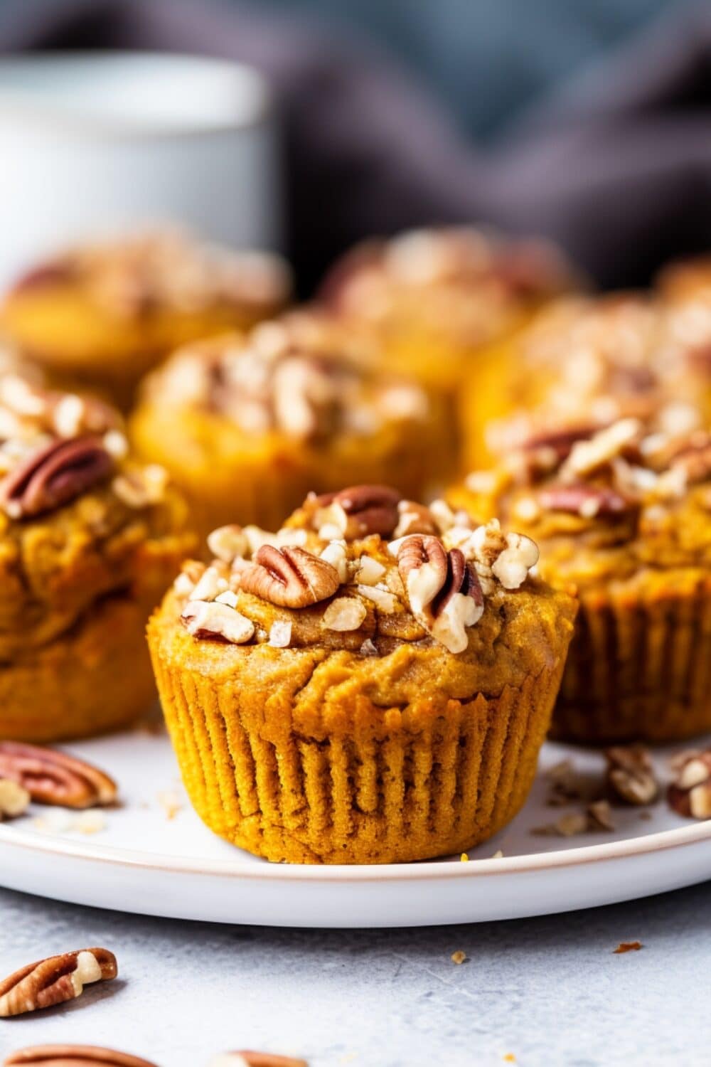 Golden-brown pumpkin muffins on a white plate, with pecans on top.