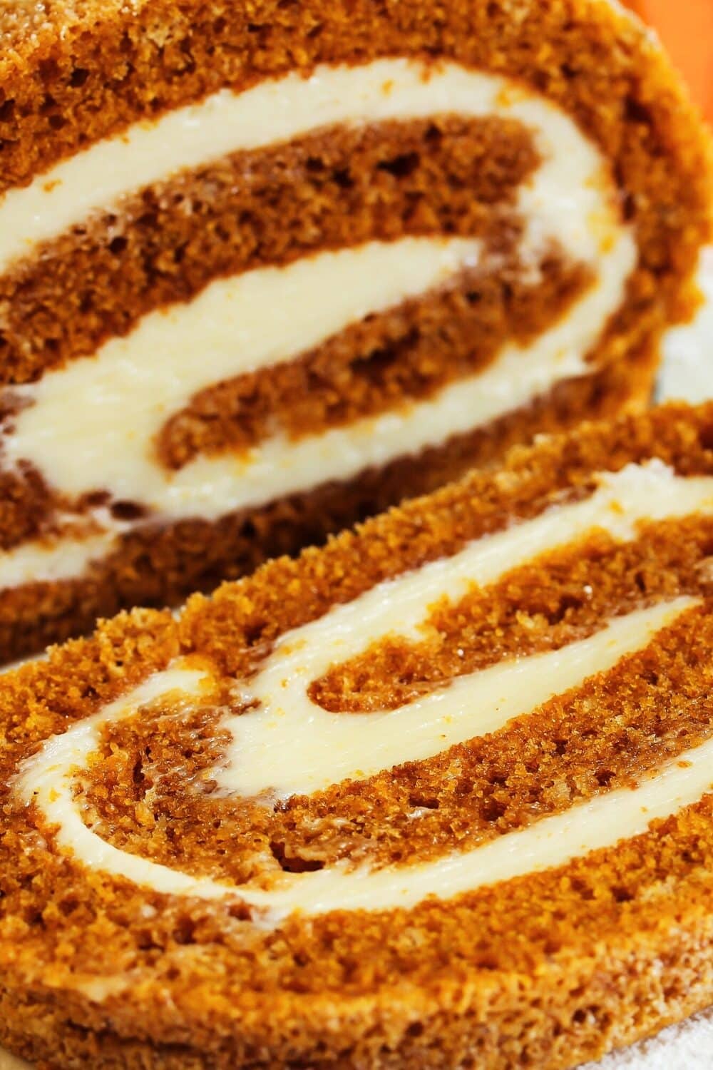 A pumpkin roll with cream cheese filling, sliced and displayed on a long plate.