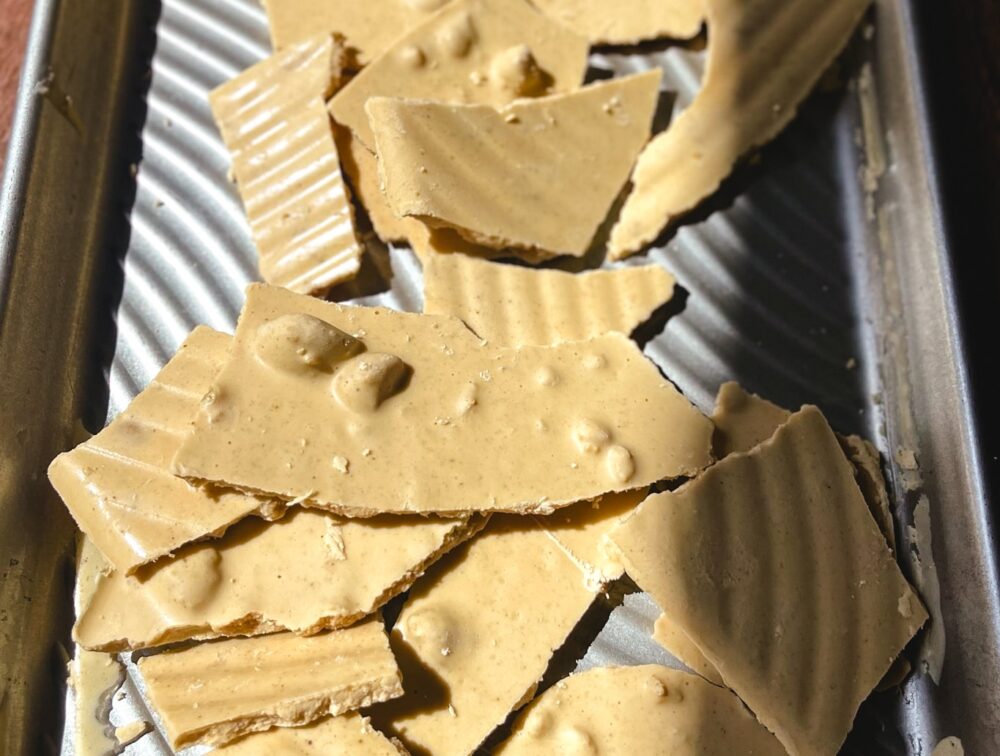 Keto-friendly peanut butter bark in broken up pieces on a baking sheet, showcasing its rich texture and tempting appearance.