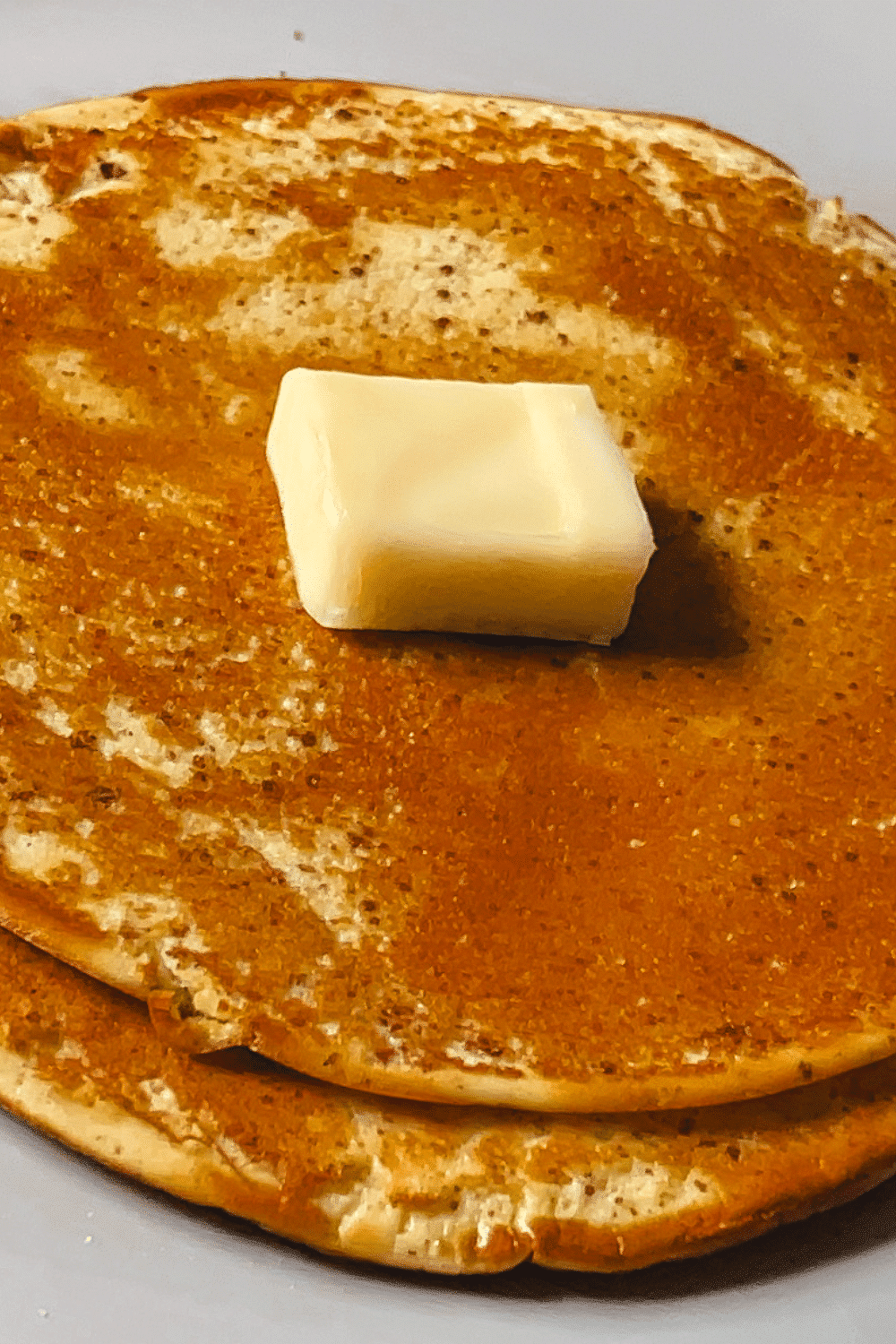 keto cream cheese pancakes served on a white plate with a large yellow pat of butter on top ready to eat