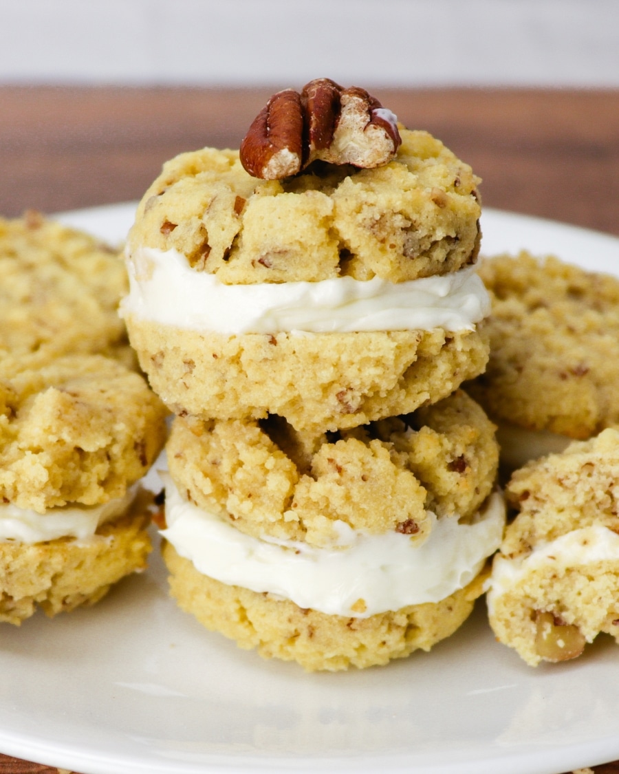 Keto pecan cookies with cream cheese filling piled on a white plate with an extra pecan on top