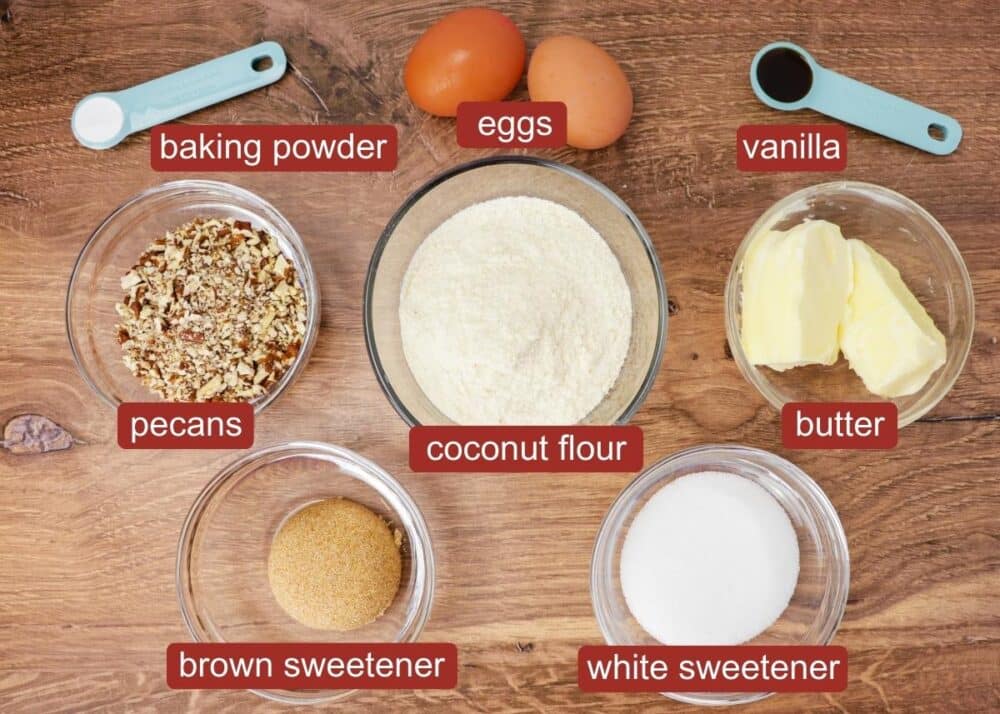 Ingredients for keto pecan cookies with cream cheese filling including baking powder, egg, vanilla, pecans, coconut flour, butter, brown sugar-free sweetener, and white sugar-free sweetener laid out in mini glass bowls, overhead shot